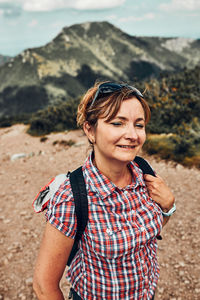 Smiling happy woman with backpack hiking in a mountains, actively spending summer vacation