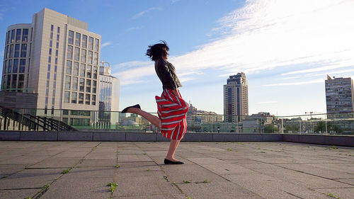 Happy woman wearing striped skirt and jacket on footpath in city