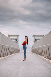 Full length of woman standing on railing against sky