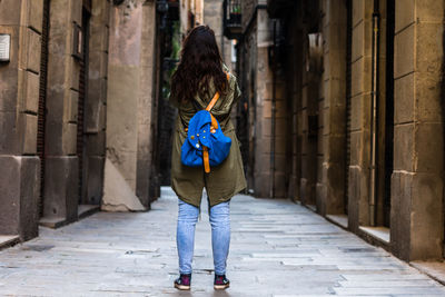 Rear view of woman carrying backpack standing on footpath amidst buildings