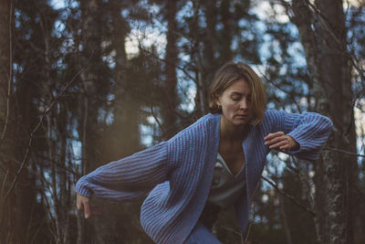 Young woman with short hair dancing against trees in forest