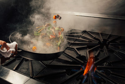 Cropped hand tossing vegetables in cooking pan over stove in kitchen at home