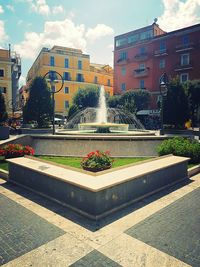 Fountain by building in city against sky