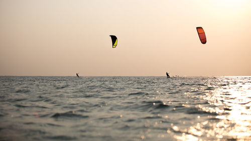 People in sea against clear sky during sunset