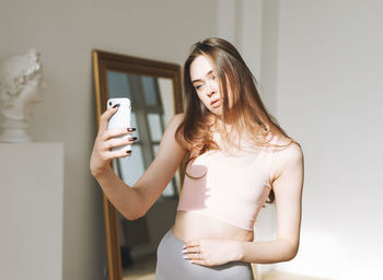 Beautiful young woman with long hair in sport wear taking selfie using mobile in studio 