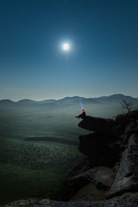 Silhouette person sitting on cliff against sky at night