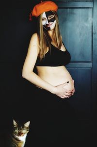 Smiling pregnant woman with face paint standing with hands on stomach against door at home