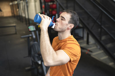 Athlete man drinking water while standing in exercise room