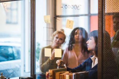 Businesswoman planning strategy on glass wall with colleagues at creative office