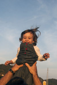 Cropped hands of father lifting cheerful daughter against sky