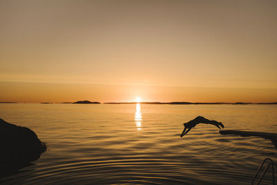 Silhouette of woman jumping into sea