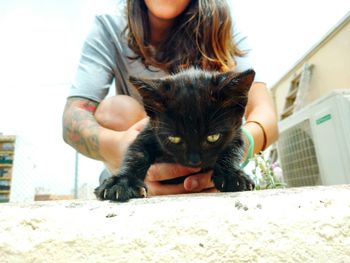 Surface level view of woman holding black kitten on footpath