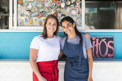 Portrait of confident young multi-ethnic female owners standing with arms around against food truck