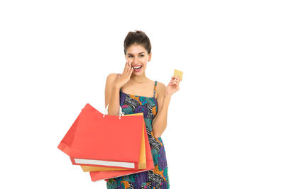 Happy young woman holding credit card and shopping bags against white background