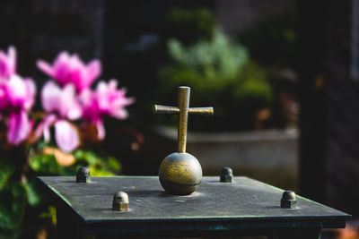 Close-up of a cross symbol sculpture in a graveyard or cemetery with flowers in the background 