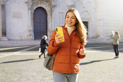 Young woman holding mobile phone while standing in city