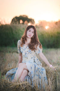 Portrait of young woman sitting on grass during sunset