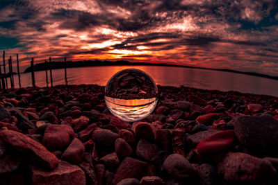 Pebbles on rocks at beach against sky during sunset