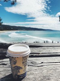 Coffee cup on table by sea against sky