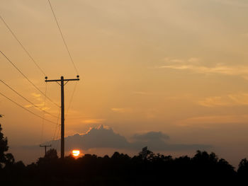 Silhouette trees and electricity pylon against sky during sunset