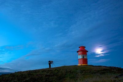 Lighthouse on field against cloudy sky