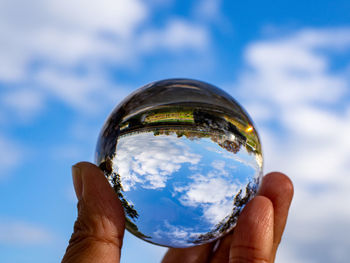 Cropped image of hand holding crystal ball against sky
