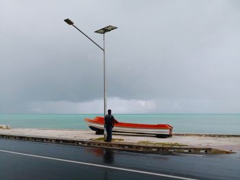 Full length of man standing by street light against sea and sky