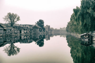 Reflection of houses and trees by lake against sky