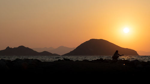 Silhouette man on beach against orange sky