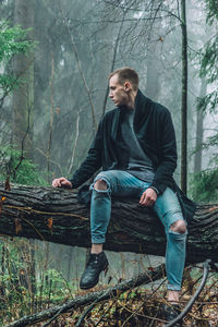Portrait of young man standing on tree trunk
