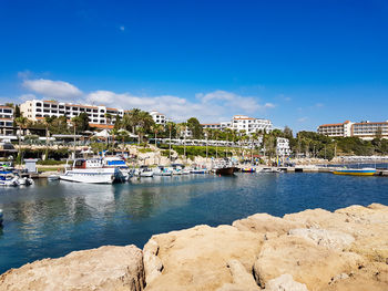 Boats moored in harbor by buildings against blue sky