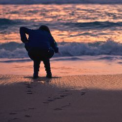 Rear view of silhouette man walking on beach during sunset