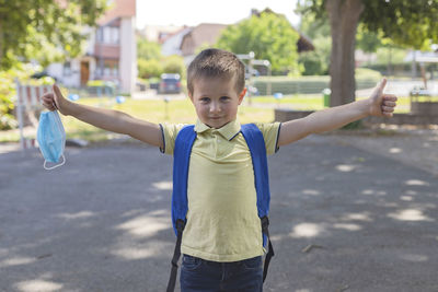 Boy wearing a protective mask with a backpack behind his back in the schoolyard 
