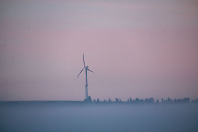 Wind turbines on landscape against sky during sunset