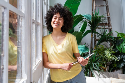 Smiling woman with digital tablet leaning on window