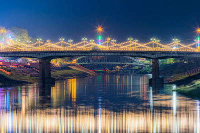 Illuminated bridge over river against sky at night