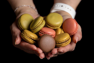 Close-up of hand holding macarons against black background