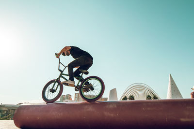 Man riding bicycle on red metallic pipe against sky