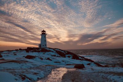 Lighthouse by sea against sky during sunset