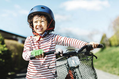 Happy boy looking away while standing with bicycle on footpath at yard