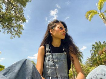 Low angle view of young woman looking away against sky