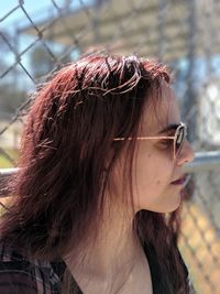 Woman wearing sunglasses looking away against chainlink fence