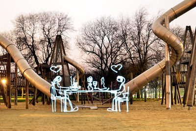 Bare trees in playground against sky