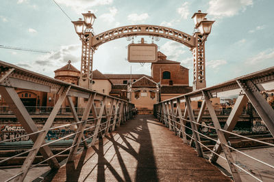 Footbridge over river in city against cloudy sky