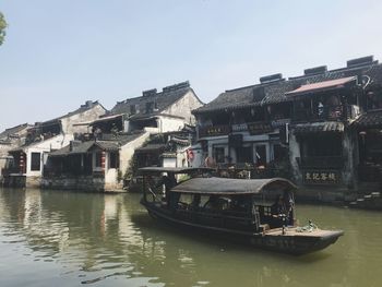 Boats in river by buildings in city against sky