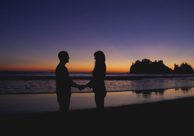 Silhouette couple holding hands at beach against clear sky during sunset
