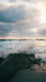 Waves splashing at beach against sky during sunset