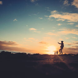 Silhouette men standing on land against sky during sunset