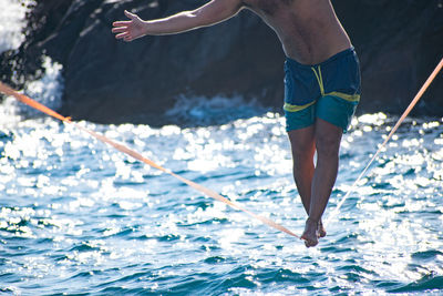 Low section of man walking on rope over sea