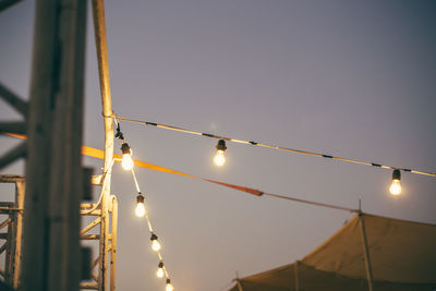 Low angle view of hanging lights against sky at sunset